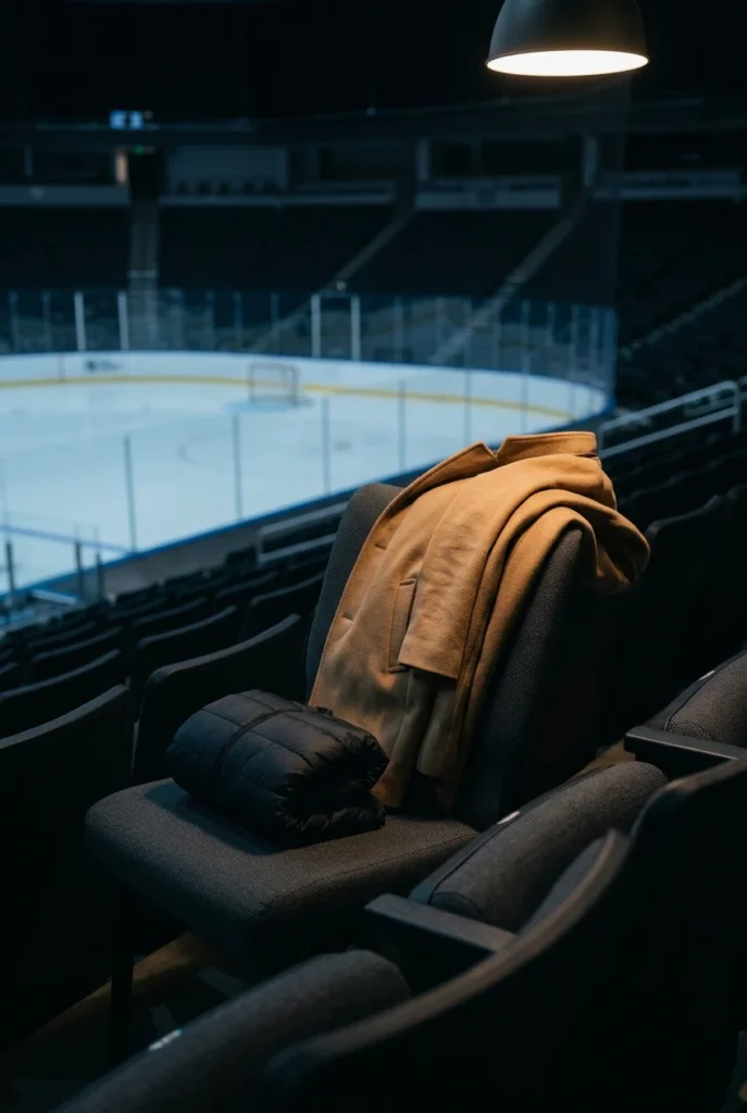 Camel wool coat and packable puffer on arena seats, hockey game outerwear options.