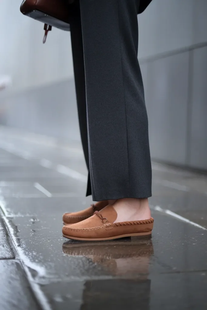 Chestnut Ugg Tasman slip ons styled with charcoal wool wide leg trousers on wet city pavement