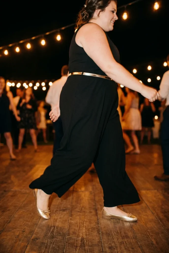 Plus size New Year's Eve outfit with black wide-leg jumpsuit, gold belt, and metallic ballet flats