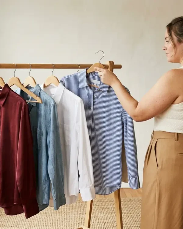 Plus-size woman choosing between four button-down shirts on a wooden garment rack